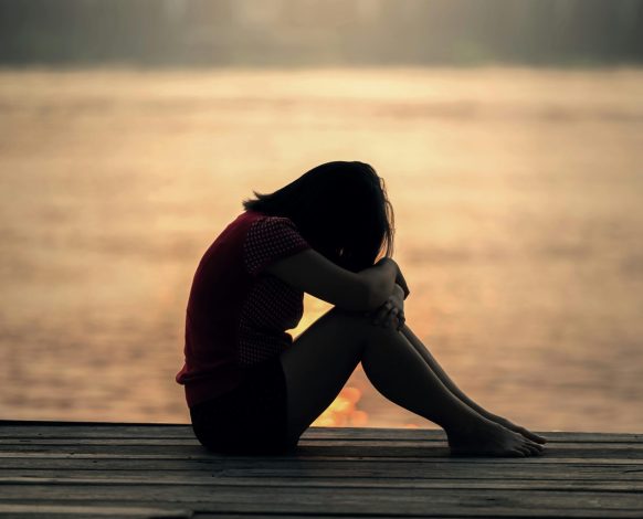 A grieving woman sitting alone at sunset, reflecting the weight and stillness of loss.