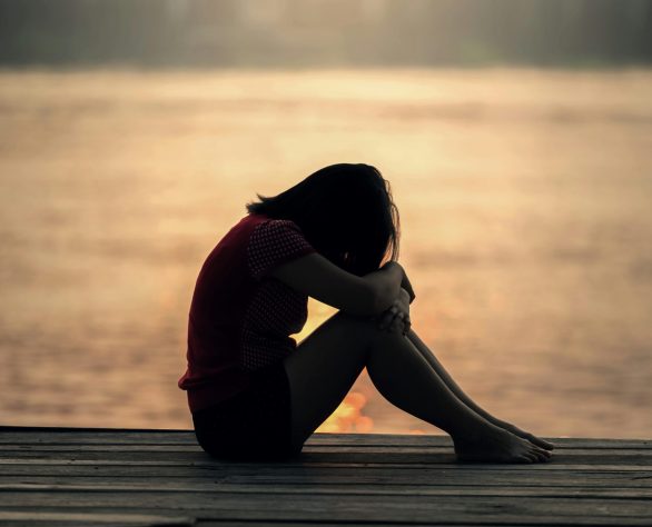 A grieving woman sitting alone at sunset, reflecting the weight and stillness of loss.