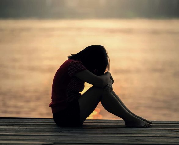 A grieving woman sitting alone at sunset, reflecting the weight and stillness of loss.